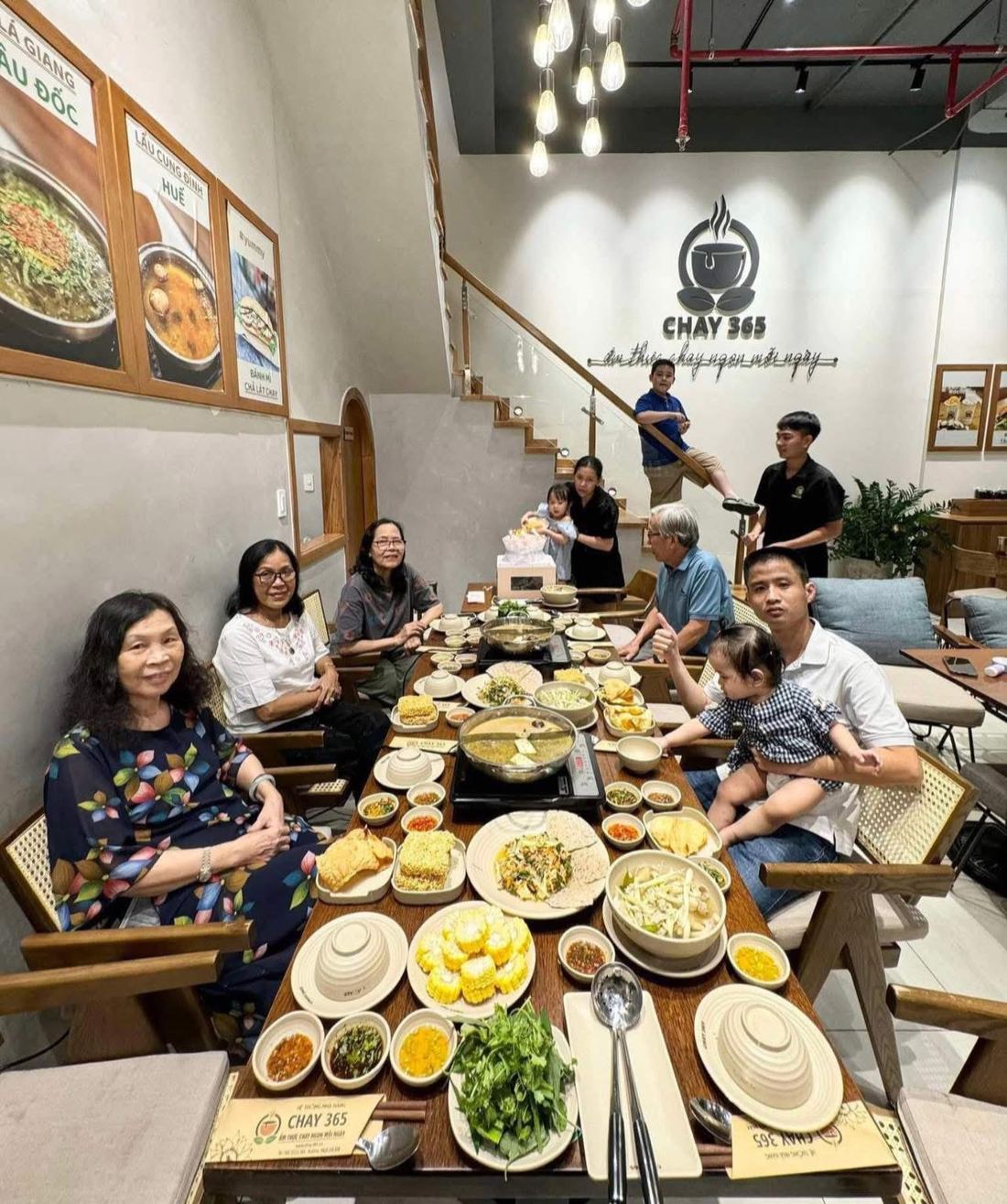 Bữa lẩu chay gia đình tại Thế Giới Lẩu Chay - Chay 365 với poster Lẩu Lá Giang Châu Đốc và Cung đình Huế trên tường